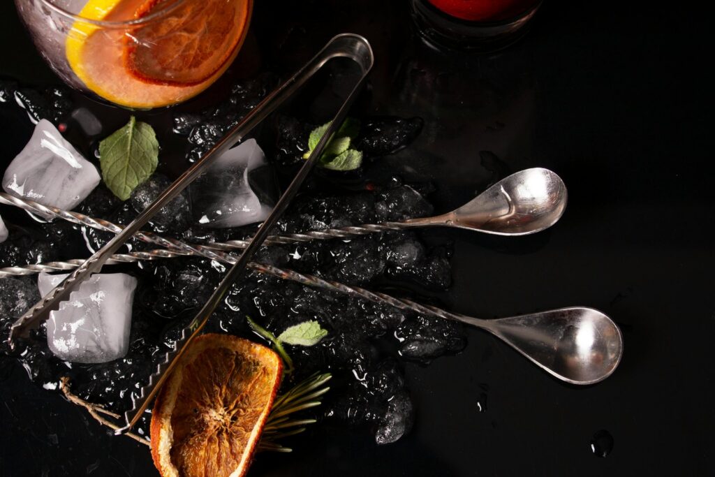 Citrus cocktail ingredients and bar tools on a dark surface